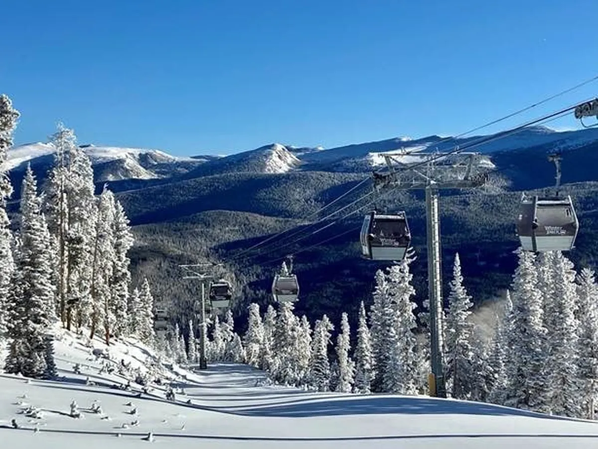 A serene winter landscape featuring ski lift gondolas gliding above snow-covered trees, with majestic mountain peaks in the distance. The setting is calm and breathtaking, inviting viewers to imagine scenic gondola rides and the thrill of the upcoming ski adventure.