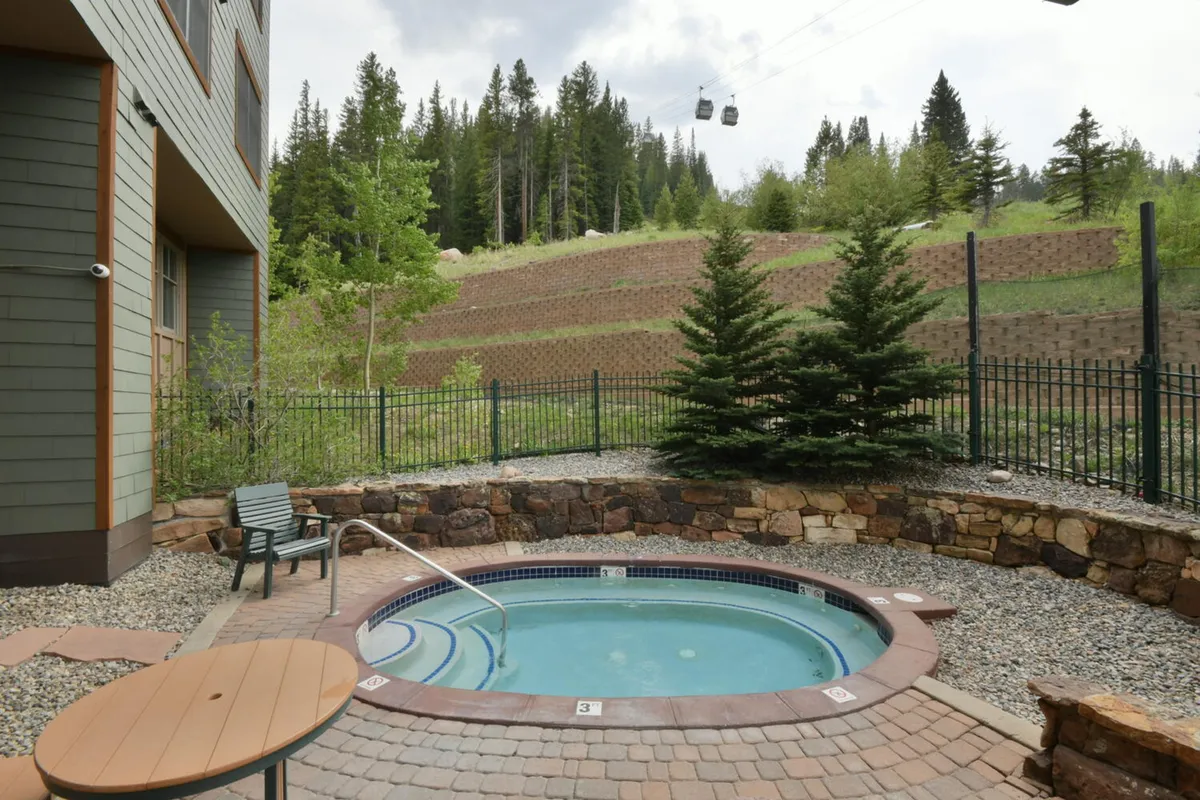 This exterior shot captures a hot tub surrounded by lush greenery with mountain views in the background. Comfortable outdoor seating and a wooden fence create a tranquil, rejuvenating atmosphere, perfect for relaxing after a day of adventure.