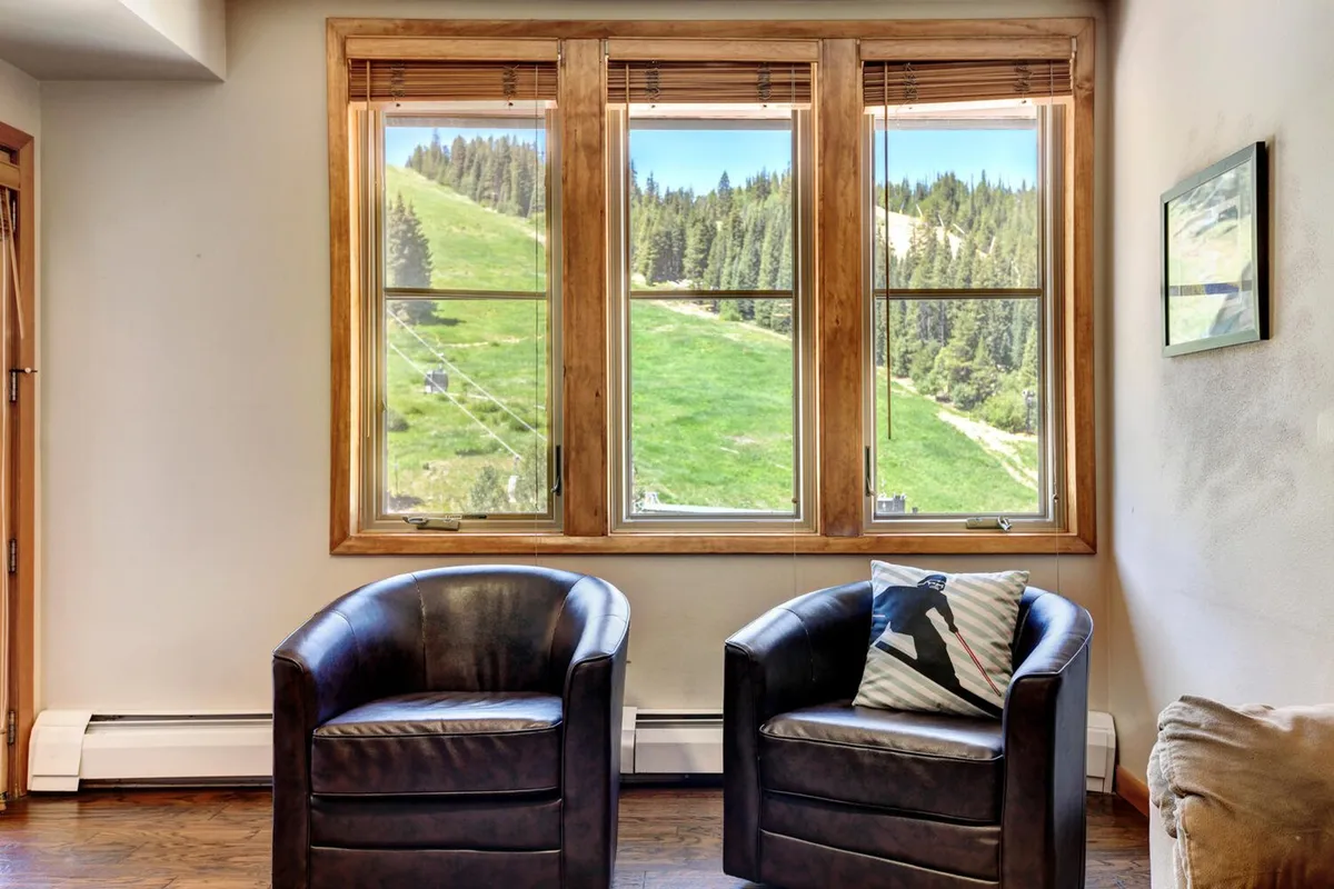 A serene corner of the living room with leather chairs, a decorative pillow, and expansive windows framing stunning mountain views. The arrangement invites quiet moments of reading, conversation, or simply soaking in the scenery and evening light.