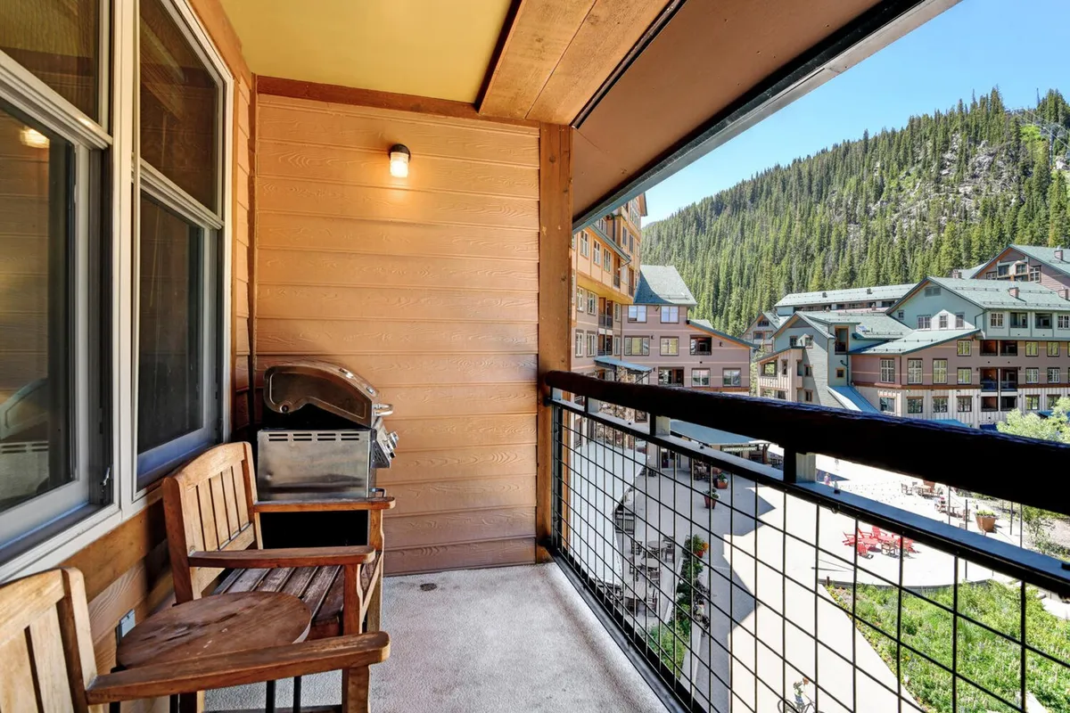 The outdoor deck features a balcony railing, a grill for barbecues, and wooden chairs arranged for relaxation. The setup is oriented toward mountain views, making it ideal for sipping coffee in the morning or enjoying sunset dinners overlooking the slopes.