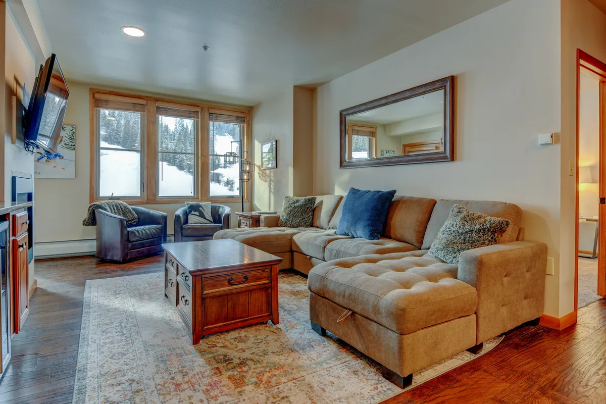 A welcoming living space with a plush sofa, coffee table, and large windows accented by decorative touches. The room exudes warmth and comfort, suggesting casual gatherings, morning coffee rituals, and intimate family time—all with a backdrop of natural light.